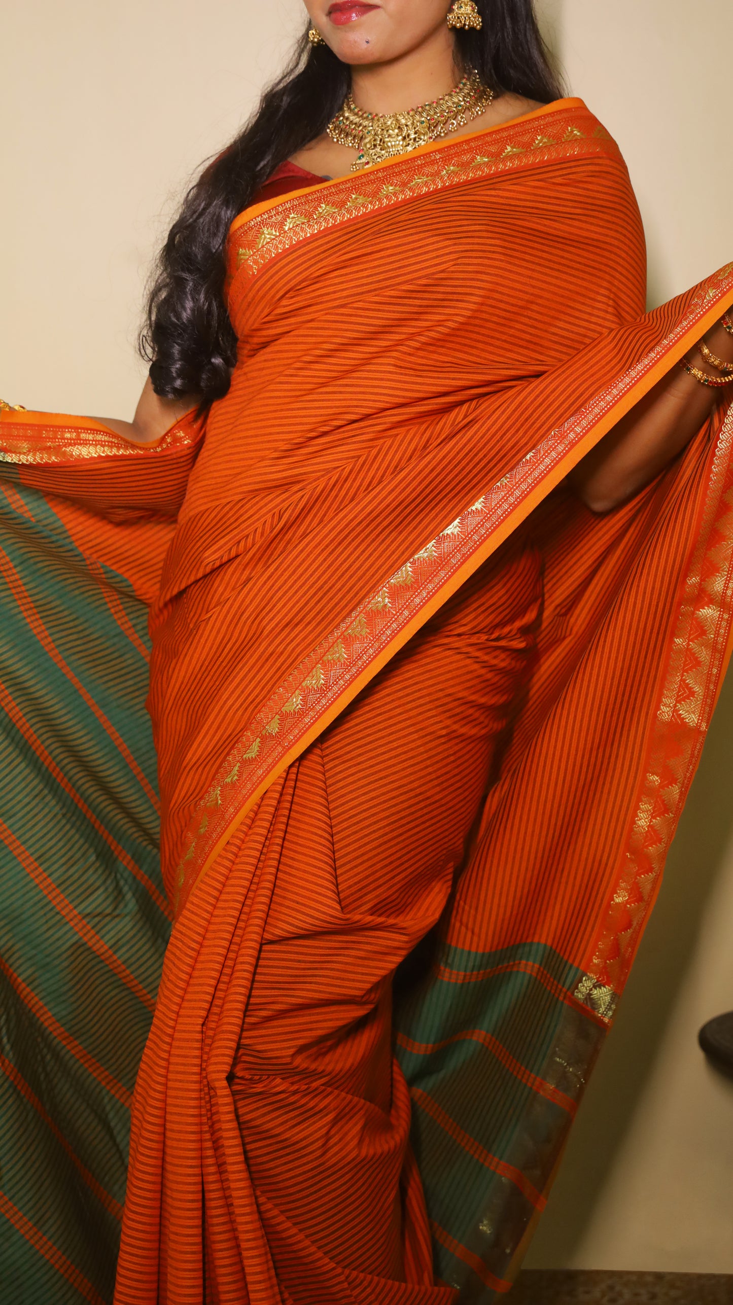 Striking rust-orange saree with fine black pinstripes and a contrasting green pallu with textured zari border and playful tassels- VARSHIKA