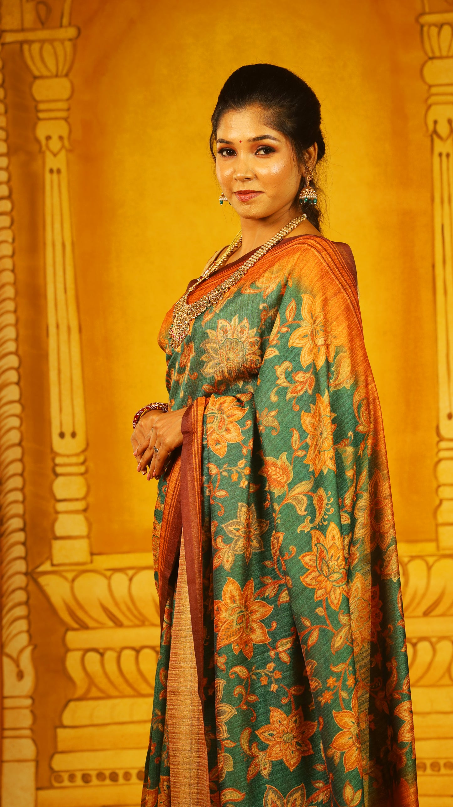 Artistic green saree with bold floral motifs and a textured ombré rust-orange base. Finished with a dual-toned pallu and tassels, offering a rich, earthy elegance. - BOOMIKA