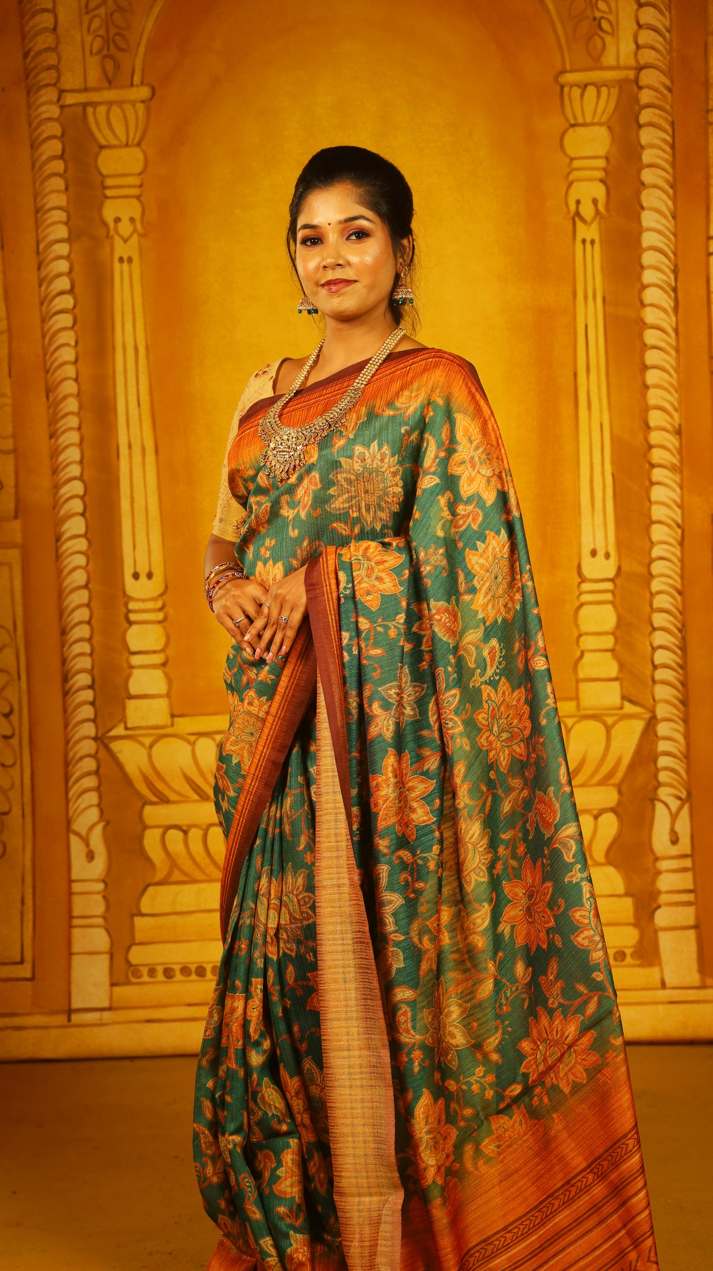 Artistic green saree with bold floral motifs and a textured ombré rust-orange base. Finished with a dual-toned pallu and tassels, offering a rich, earthy elegance. - BOOMIKA